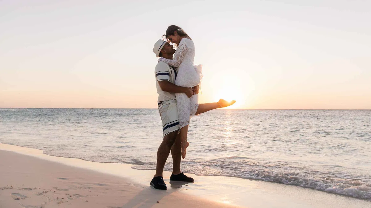 A photographer directing a couple on a white-sand beach during a private Aruba photoshoot at sunset, Aruba